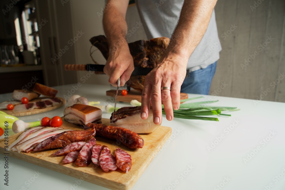 Cook's hands cut pork delicacies, prosciutto, lard, sausage, Bavarian sausages