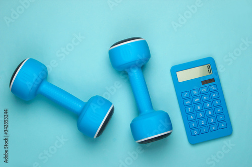 Fitness, weight loss still life. Calorie Counting. Calculator and dumbbells on blue pastel background. Minimalism. Flat lay