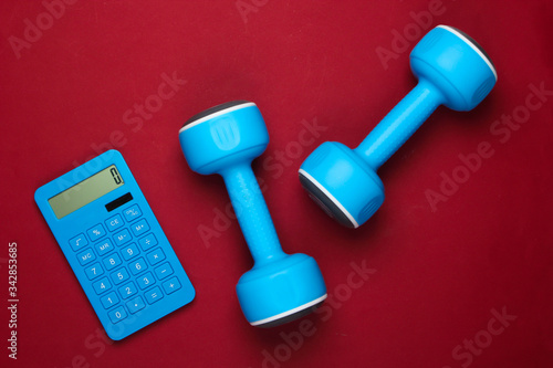 Fitness, weight loss still life. Calorie Counting. Calculator and dumbbells on red background. Minimalism. Flat lay