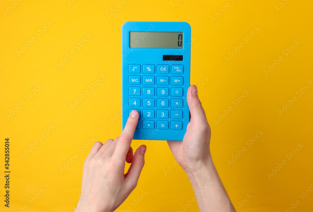 Hand holds blue calculator on yellow background. - obrazy, fototapety, plakaty 