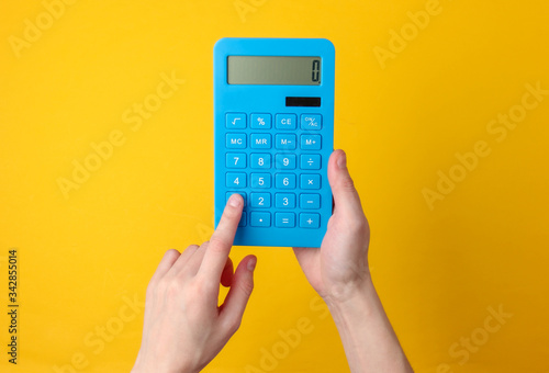 Hand holds blue calculator on yellow background. photo
