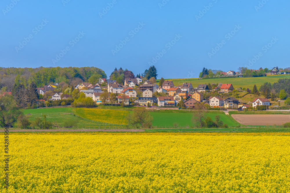 The settlement of Anhausen near Herbrechtingen in Baden-Württemberg, Germany. Small german village. Blue sky, bright-yellow rapeseed field in the foreground. Travel, agriculture concept The settlement of Anhausen near Herbrechtingen in Baden-Württemberg, Germany. Small german village. Blue sky, bright-yellow rapeseed field in the foreground. Travel, agriculture concept