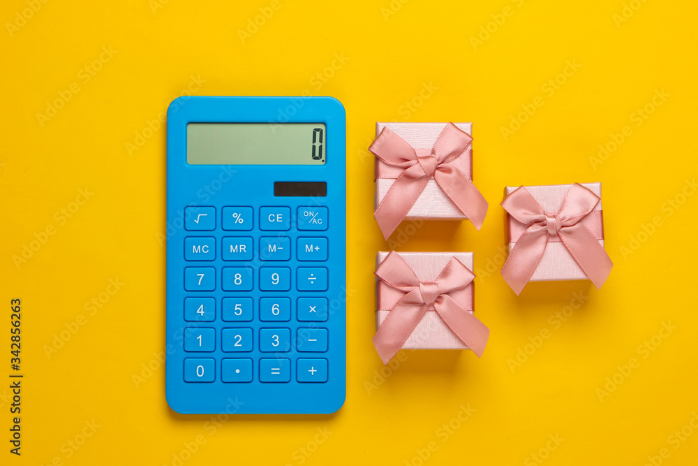 Calculator and gift boxes with bow on yellow background. Calculation the value of gift. Top view. Calculator and gift boxes with bow on yellow background. Calculation the value of gift. Top view.