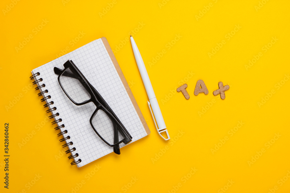 Word tax and notebook with glasses on yellow background. Top view Word tax and notebook with glasses on yellow background. Top view