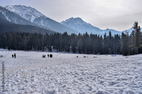 Snow field covered with snow forest with himalayas mountains in the backdrop in Pahalgam. People enjoying skateboarding in snow field on Christmas and New year holidays celebration in Kashmir, India. 