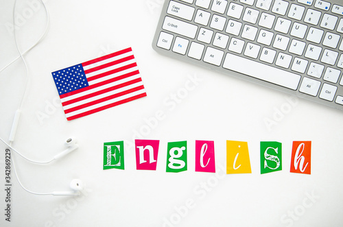 USA flag and word ENGLISH on a white desktop with keyboard and earphones. Flat lay Learn a language at home concept