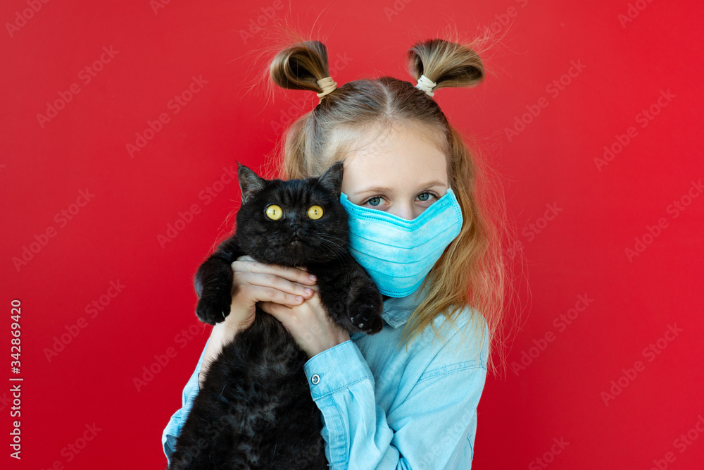 Blonde teenage girl in a protective mask holds her cat and looks at the camera on a red background. Isolation, coronavirus, stay home. Blonde teenage girl in a protective mask holds her cat and looks at the camera on a red background. Isolation, coronavirus, stay home.