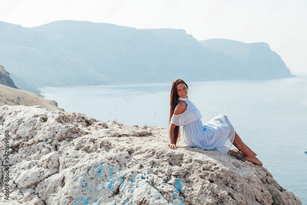beautiful woman with long hair in dress on cliff cliff by the sea