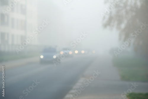 Out of focus cars riding on a city street in a foggy autumn morning