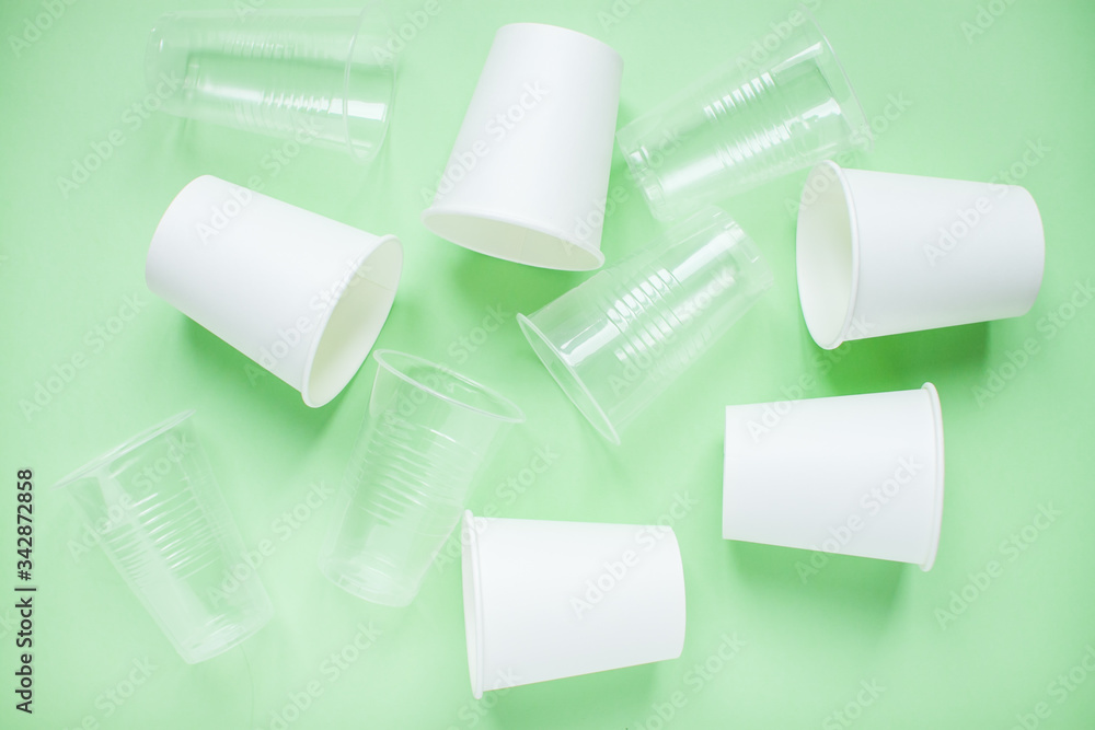 Obraz premium The layout on a green background from white paper and plastic disposable cups. Caring for the environment. Recycling and sorting of garbage. Disposable tableware. Environmental pollution.