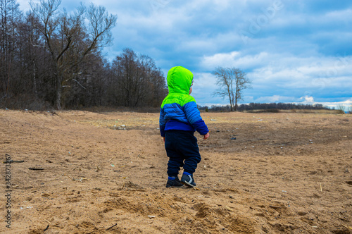 Llost little boy wanders on a muddy beach in early spring or autumn in a bright jacket with a hood on his head © smartik1988