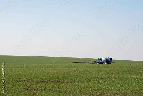 blue tractor sprinkles wheat, blue harvester sprinkles wheat, blue tractor sprinkles field from pests, tractor sprinkles green field, blue harvester in the field, irrigation combine in the field