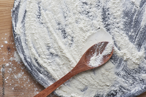 Overhead shot of used wooden chopping board and wooden spoon scattered with white flour.