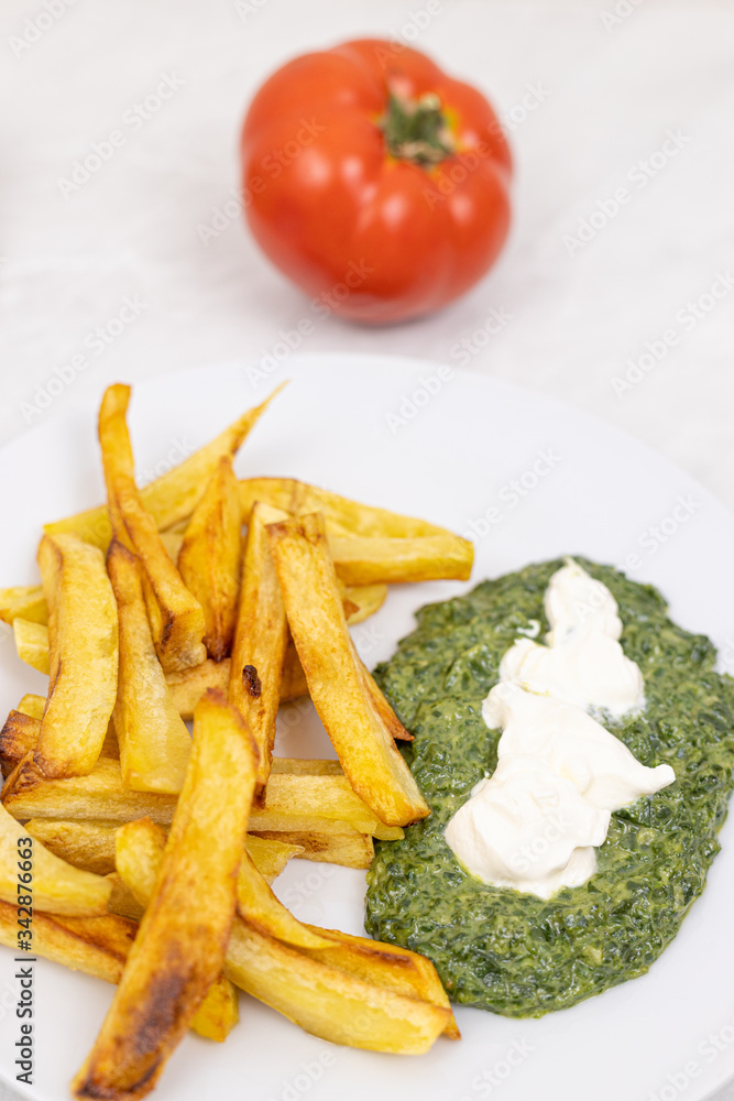 French fries and spinach on the plate with tomato in the background French fries and spinach on the plate with tomato in the background