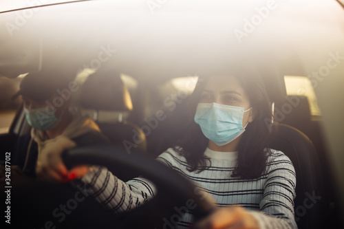 Boy and girl driving a car wearing sterile medical mask. Taxi driver with a passanger stuck in a traffic jam during coronavirus quarantine isolation in the city. Prevernt spread of covid-19 concept.