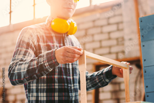 Closeup of male woodworker holding wooden beehive frame in hands while working at sawmill. Man professional carpenter working with wood production at his workshop. Young cabinet maker, woodworking