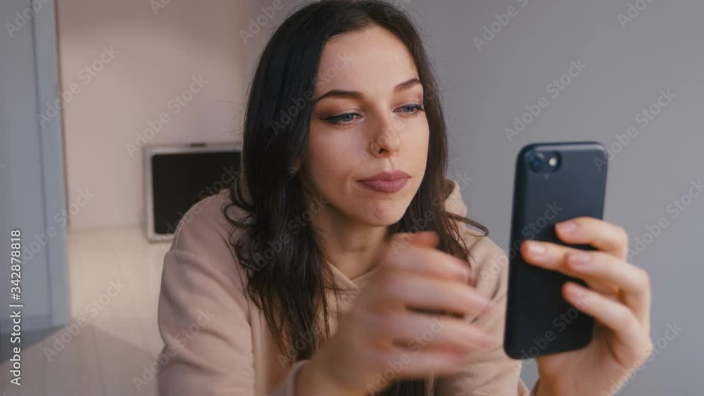 Young beautiful brunette woman using smartphone and drinking coffee at home. Smiling millennial girl looking at mobile phone screen, typing message in social network, shopping online, web surfing. Young beautiful brunette woman using smartphone and drinking coffee at home. Smiling millennial girl looking at mobile phone screen, typing message in social network, shopping online, web surfing.