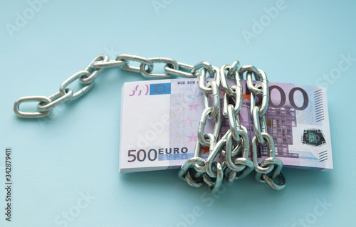 A bundle of 500 Euro banknotes is wrapped with a metal chain. The monetary savings. Selective focus.
