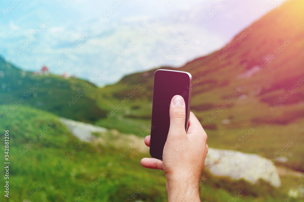 Hand holding mobile phone in mountain landscape setting