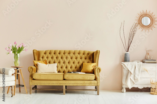 Cozy living room interior of retro armchair, vintage wooden chest dwarf and vintage couch on the background of the beige wall and painted wooden floor