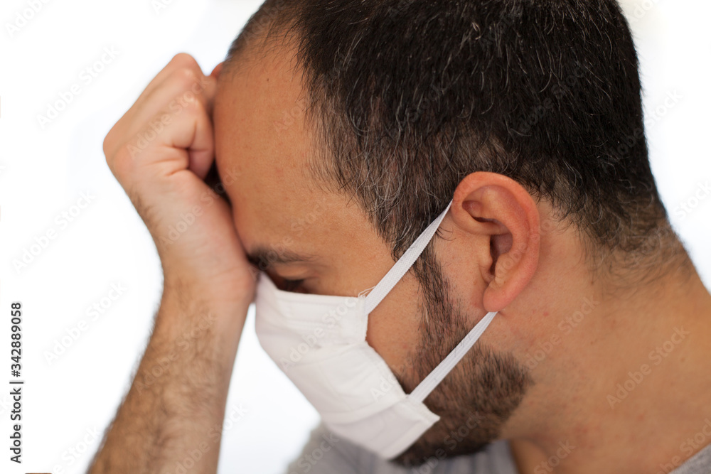 Obraz premium A man sick with coronavirus wears a mask and touches his forehead due to the symptoms he is suffering such as fever, tiredness and headache.