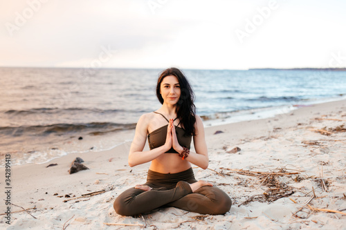 A young girl sits in a lotus position on the seashore at sunset. Girl practices yoga by the sea