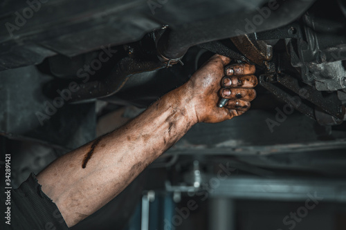 a dirty hand with a key loosens the screw on the car during repair