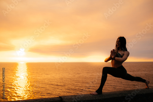 Atmospheric photo of a young girl who practices yoga at sunset by the sea
