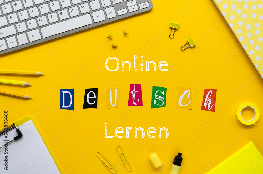 ONLINE DEUTSCH LERNEN sign on a student table framed withoffice stationery and pc keyboard. Top view on a yellow background - obrazy, fototapety, plakaty 