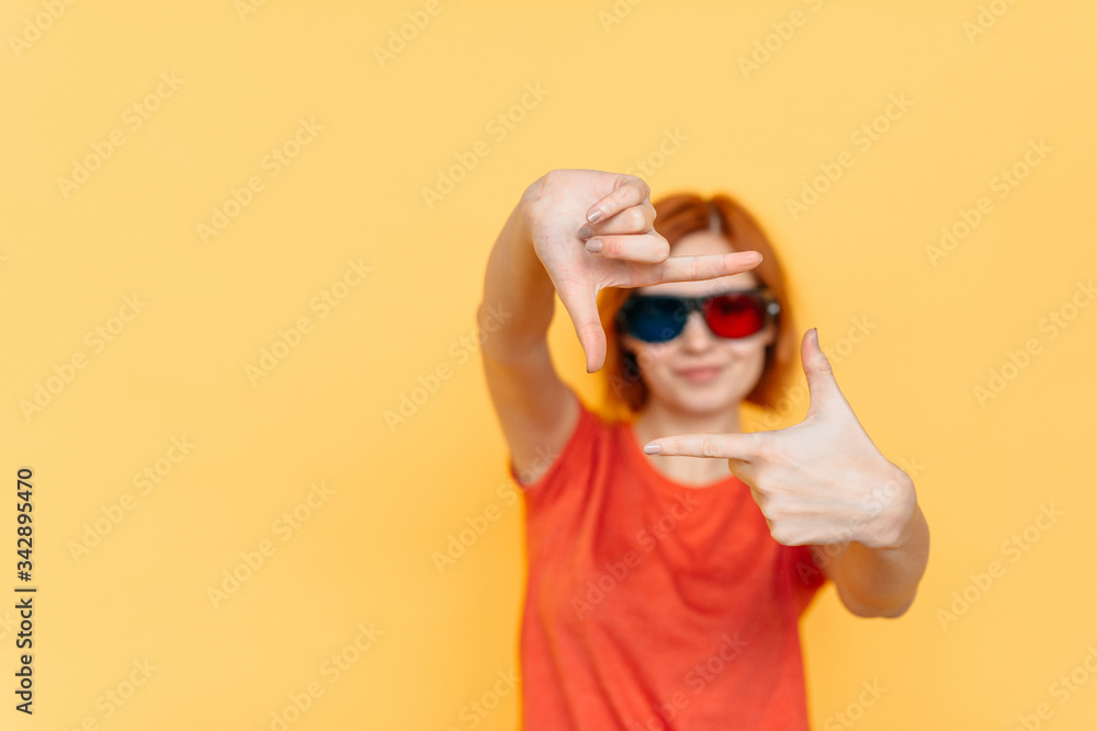 Fashionable young positive lady with red hair gesturing, making camera frame with her fingers, posing isolated on yellow background, studio shoot Fashionable young positive lady with red hair gesturing, making camera frame with her fingers, posing isolated on yellow background, studio shoot