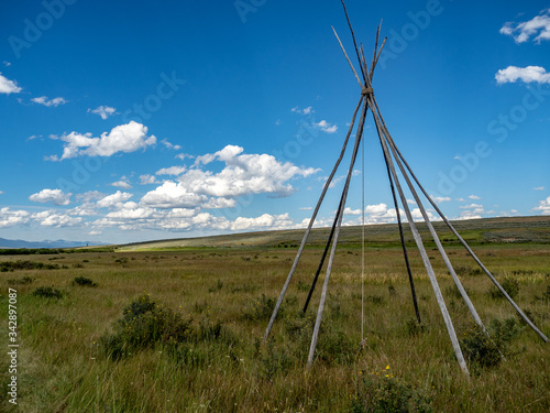 Nez Perce teepee frames with white billowing clouds and blue sky in background.