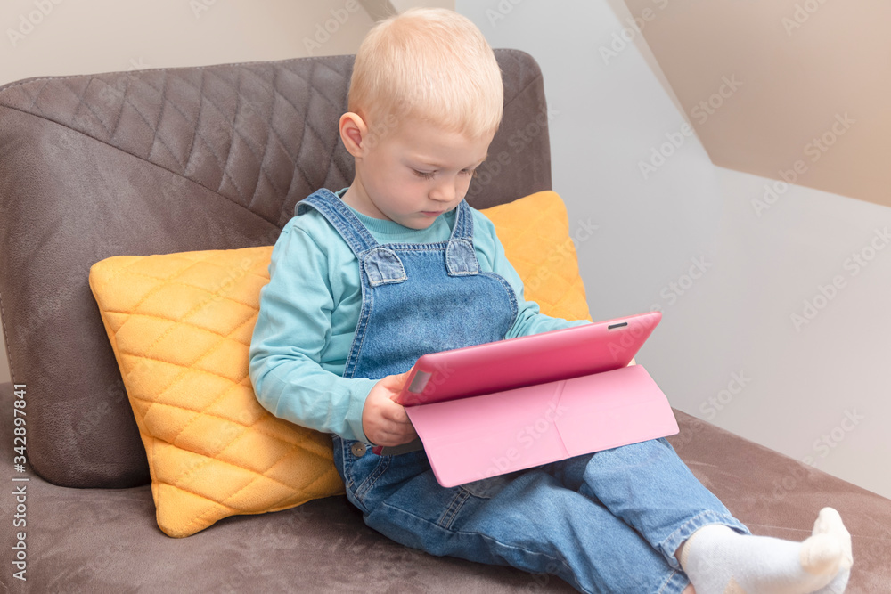 Cute toddler boy holding digital tablet and watching cartoons. Kids and technology concept Cute toddler boy holding digital tablet and watching cartoons. Kids and technology concept