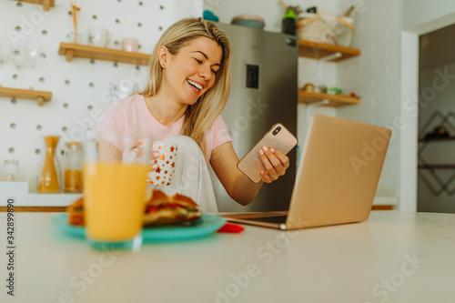 Close photo of young blonde woman with beautiful smile reading messages on her smartphone. Photo of young woman working from home quarantine.
