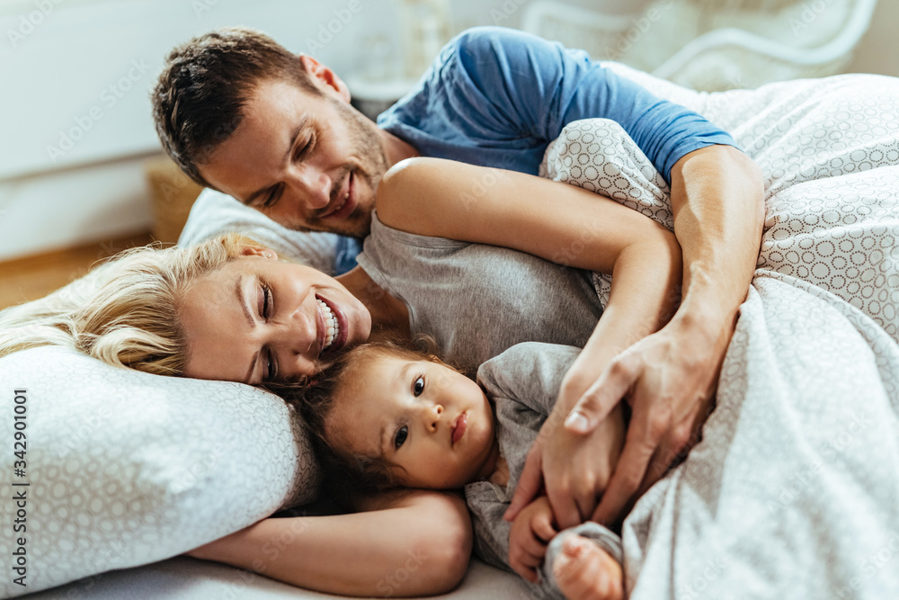 Happy parents and their small daughter relaxing in bedroom. Happy parents and their small daughter relaxing in bedroom.