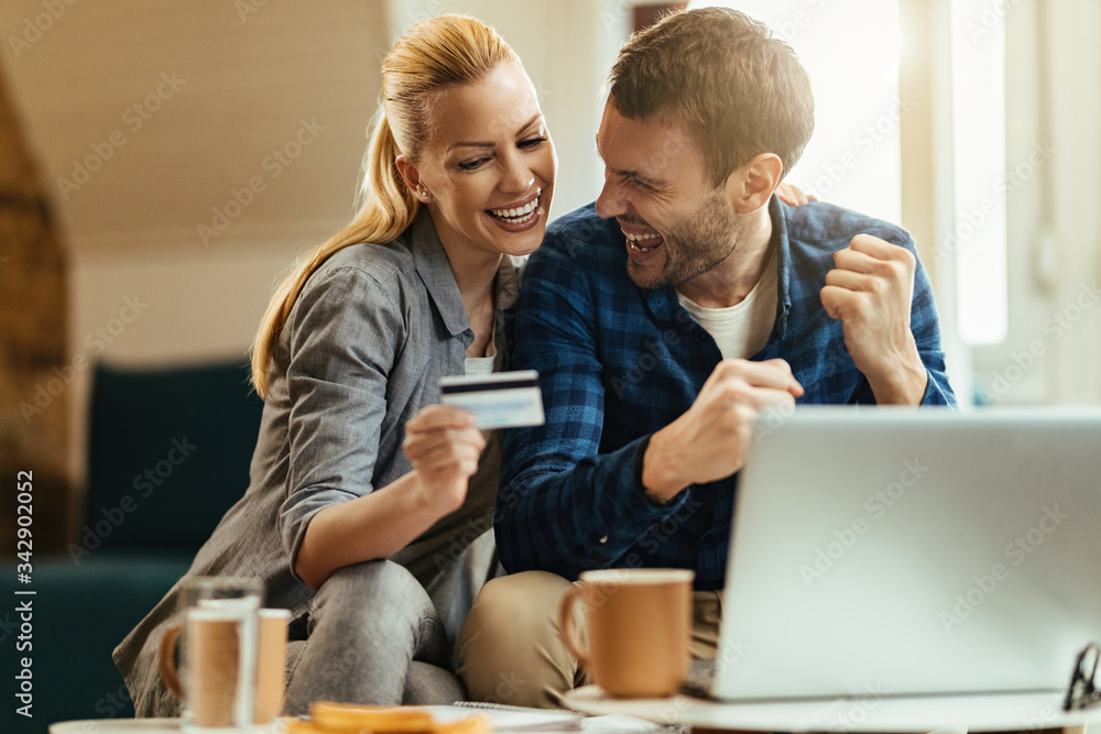 Happy couple celebrating while using credit card and online banking at home. Happy couple celebrating while using credit card and online banking at home.