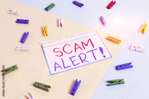 Writing note showing Scam Alert. Business concept for fraudulently obtain money from victim by persuading him Colored clothespin paper reminder with yellow blue background