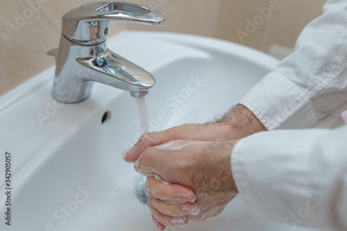 Young man washing hands at home cleaning hand under running water in bathroom sink. House, lifestyle.