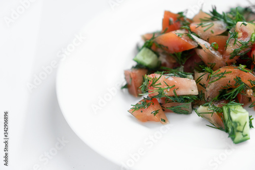 Tomato and cucumber salad sprinkled with herbs, on a white plate.
