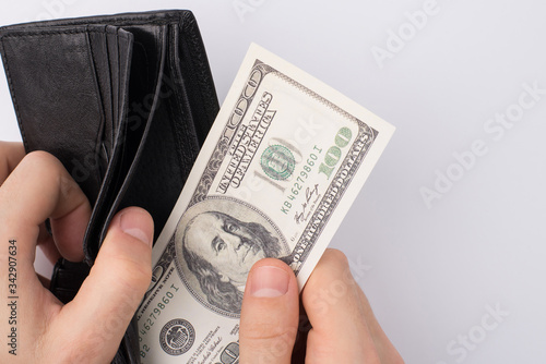 Cropped close up photo of male hands taking last 100 dollars from the leather black wallet isolated over grey background with empty space