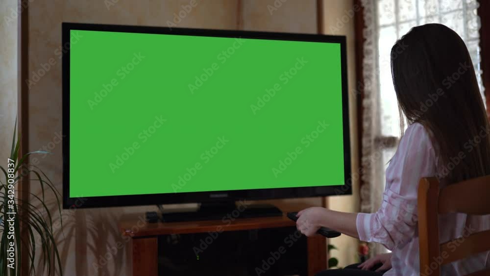Woman holding remote control and changing channels of modern TV. Large television with green screen, chroma key concept Woman holding remote control and changing channels of modern TV. Large television with green screen, chroma key concept