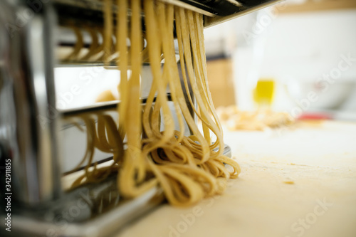Staying at home with your family and preparing fresh home-made pasta  tagliatelle   pasta machine on a wooden board cutting sheets of pasta into noodles.