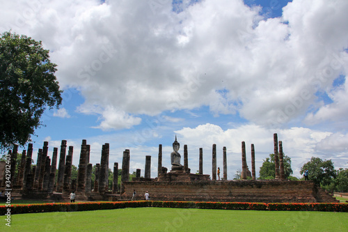 Buddha amidst columns and vegetation with sunny day in Sukhothai