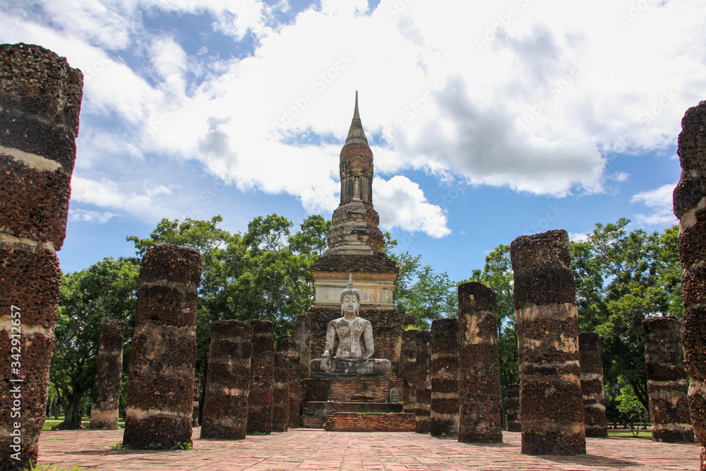 Buddha in the middle of columns and with vegetation in the background in Sukhothai