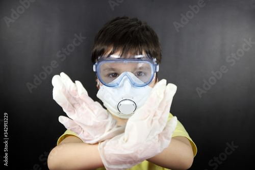 niño con mascarilla, gafas de protección y guantes  para protegerse del coronavirus diciendo basta ya  con las manos cruzadas photo