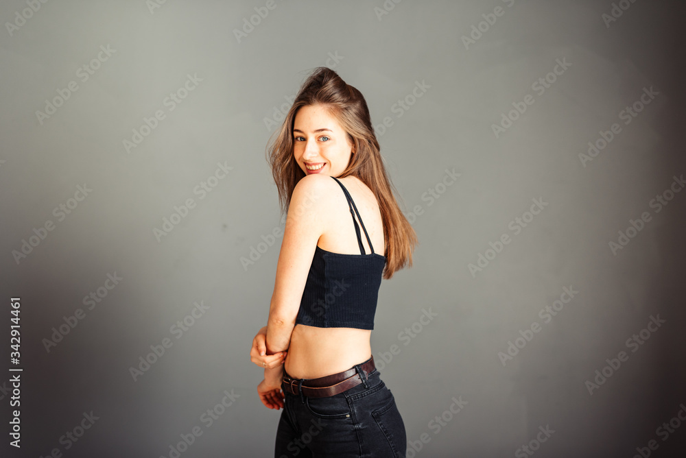 Fototapeta premium Portrait of a girl in a black top with her hair against a gray background. Without makeup, without retouching.