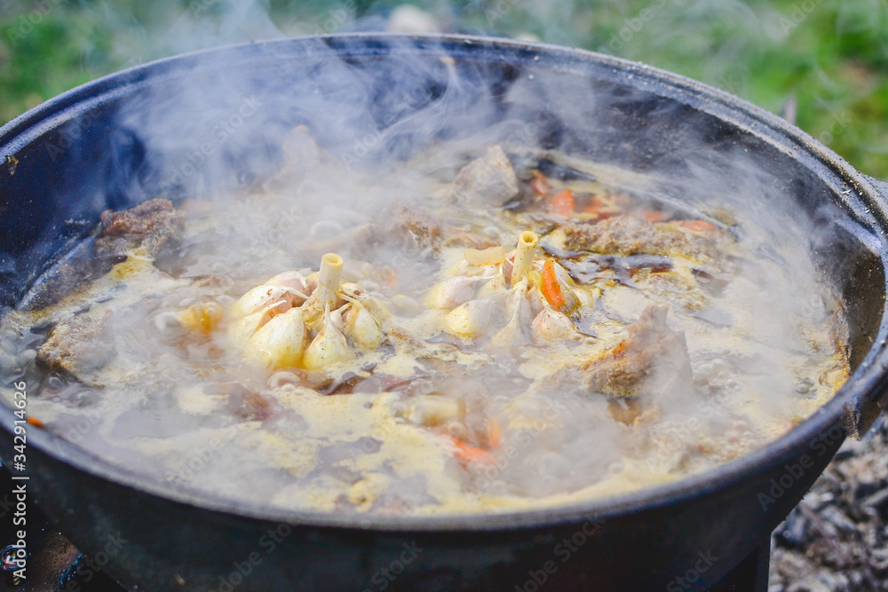 Pilaf on the cooking stage, zirvak with garlic, raisins, carrots, onions, lamb, barberry, saffron, zira and oil in a cauldron, boiling on the fire