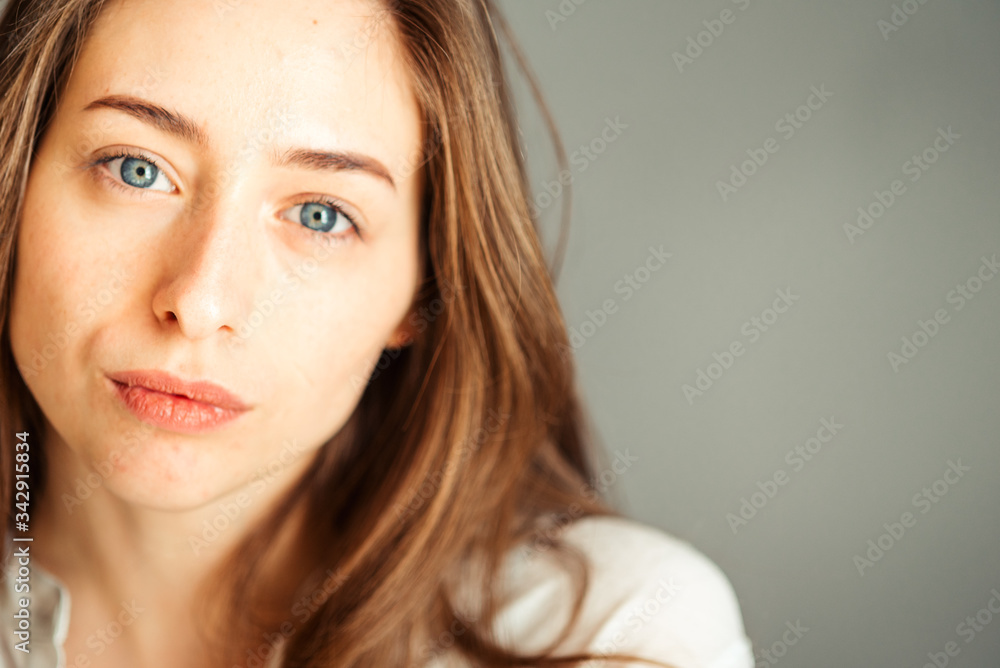 Serious girl with her hair in bright clothes on a gray background, close-up. Nude makeup, without retouching. Serious girl with her hair in bright clothes on a gray background, close-up. Nude makeup, without retouching.