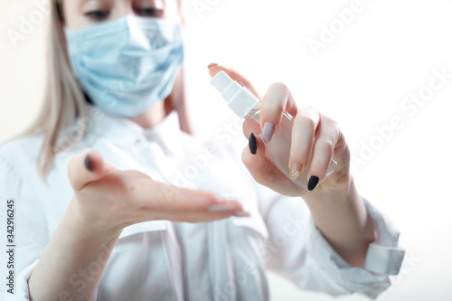 young blonde girl in a white blouse and a medical mask uses an antiseptic on a white background