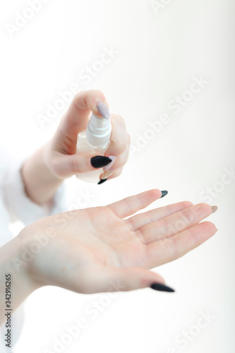 young blonde girl in a white blouse and a medical mask uses an antiseptic on a white background