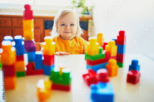 Adorable little girl playing with colorful plastic construction blocks